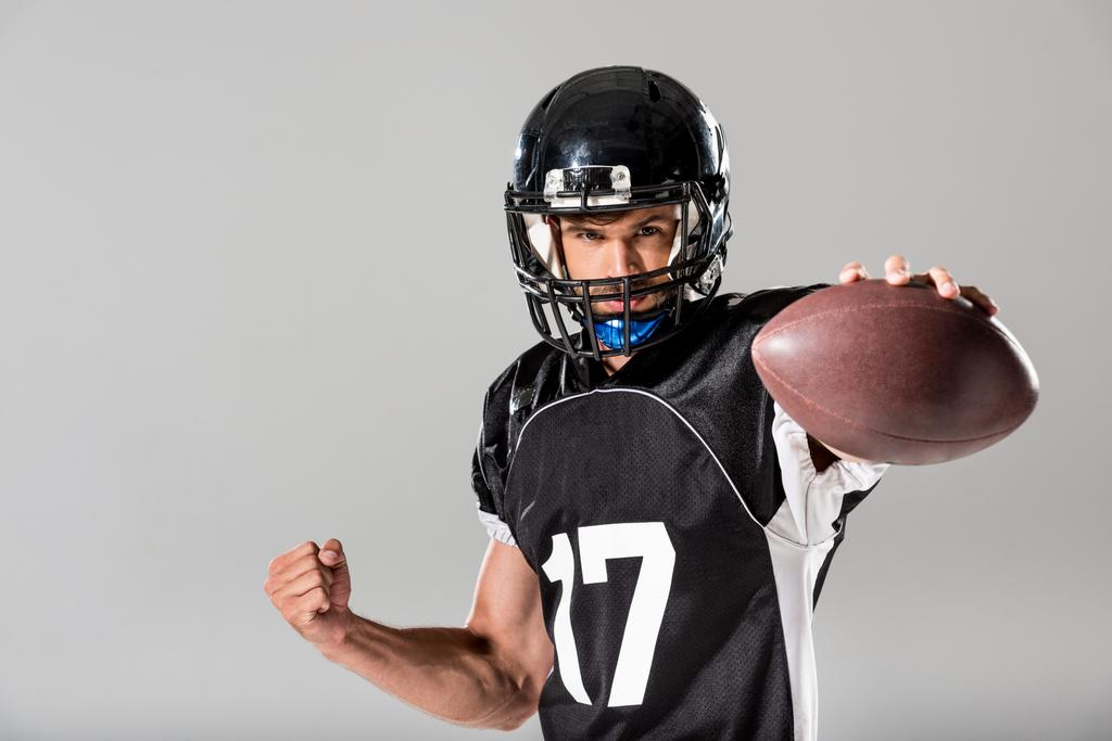 Americký fotbalový hráč v helmici s koulí izolovaný šedý - Fotografie, Obrázek