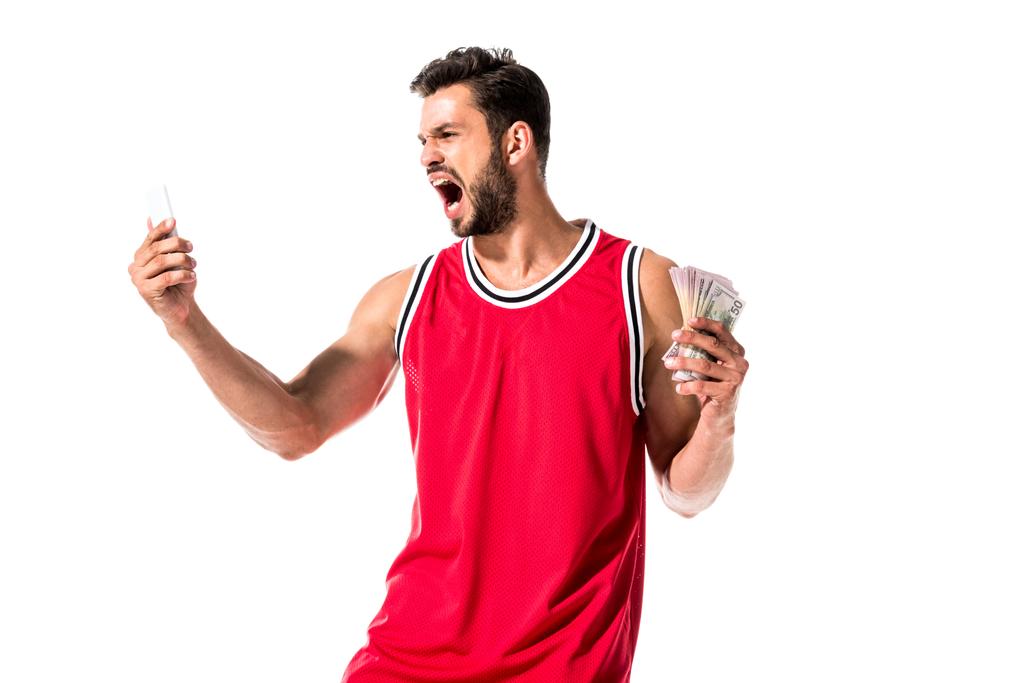θυμωμένος παίκτης μπάσκετ κρατώντας χρήματα και smartphone απομονωμένη σε λευκό  - Φωτογραφία, εικόνα