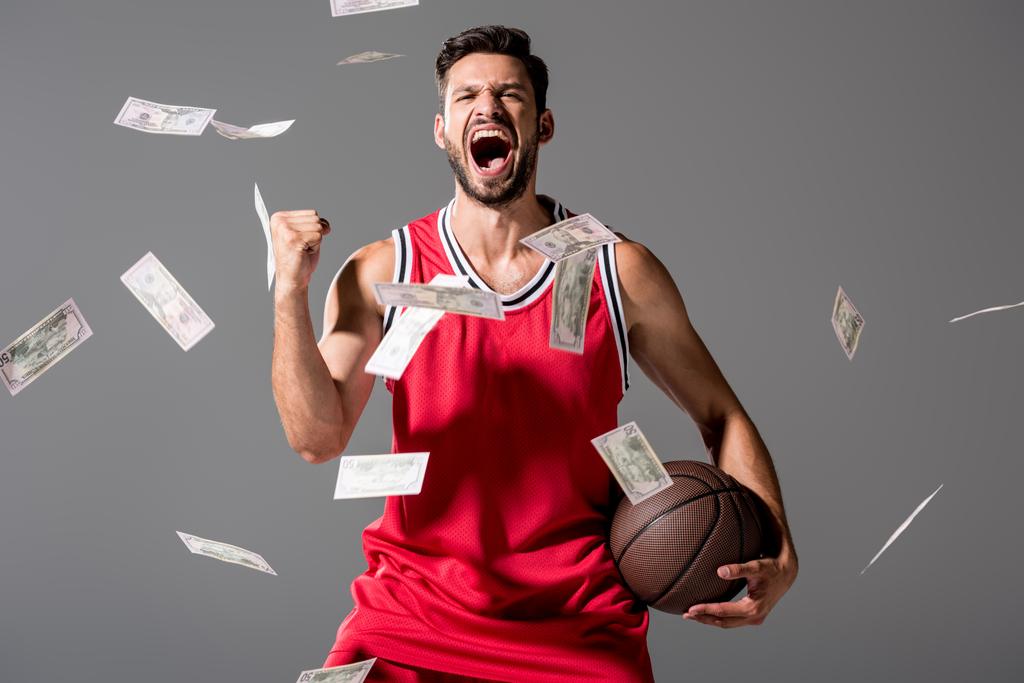 schreiender Basketballspieler mit Ball isoliert auf grau mit fallendem Geld - Foto, Bild