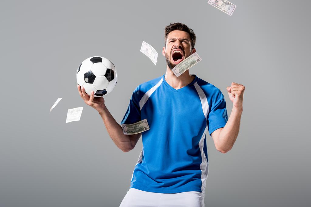 soccer player with ball cheering with clenched hand near falling money on grey - Photo, Image
