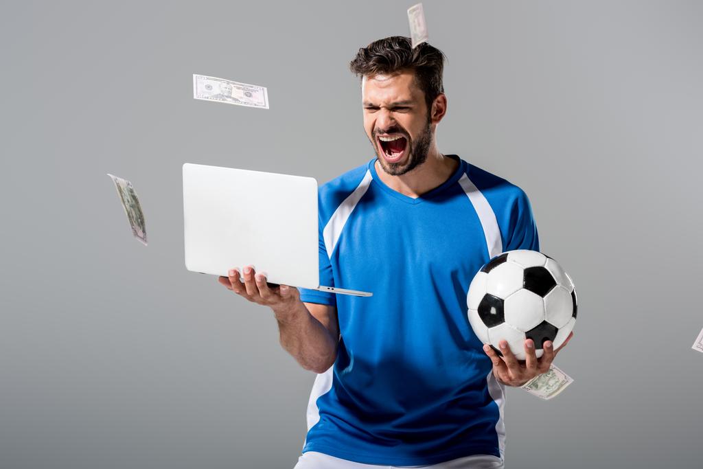 jugador de fútbol emocionado con la pelota y el ordenador portátil cerca de caer dinero en gris
 - Foto, Imagen