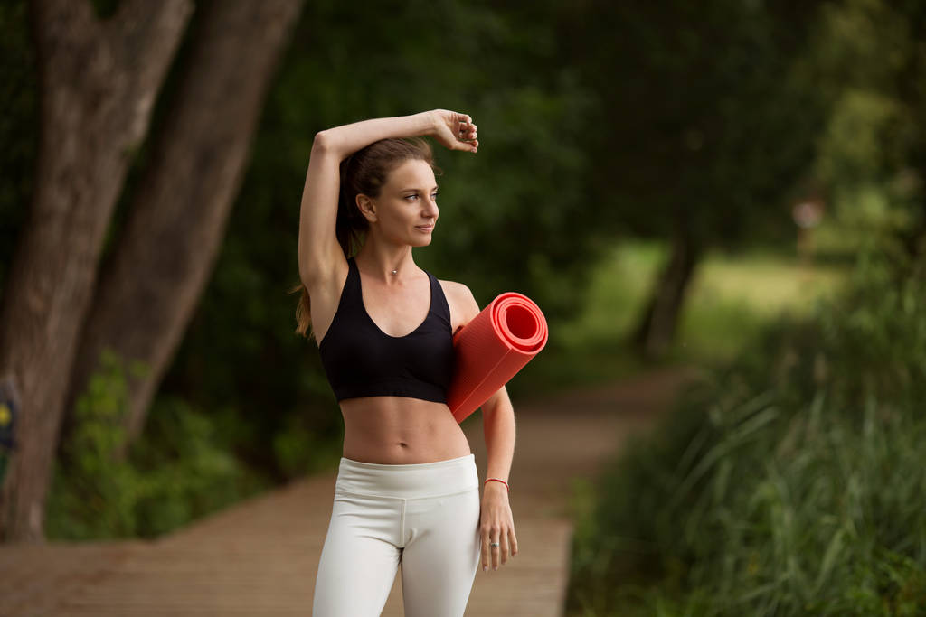 Chica bastante deportiva con esterilla de yoga al aire libre en el parque verde, hora de verano
 - Foto, Imagen