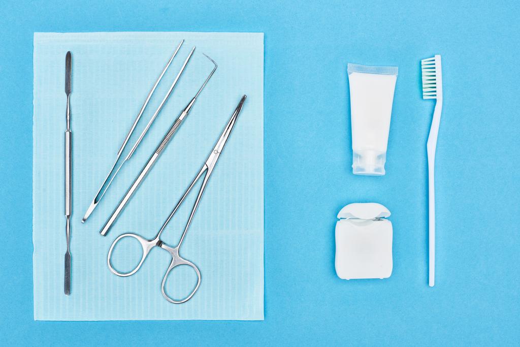 vrchní pohled na sadu s dentálními nástroji v blízkosti zubní pasty a zubního kartáčku izolovaného na modrém  - Fotografie, Obrázek