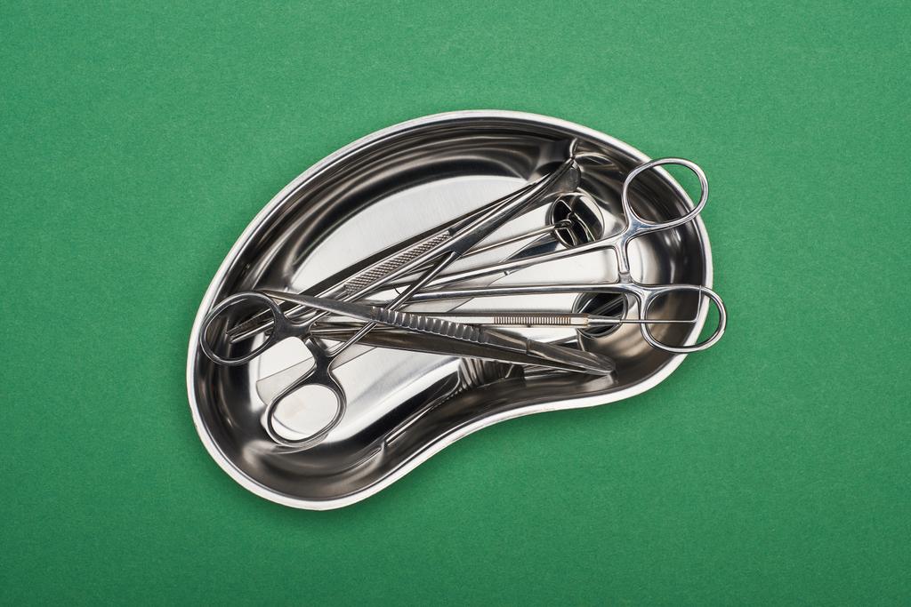 вид сверху металлической плиты с набором стоматологических инструментов и ножниц, изолированных на зеленом
  - Фото, изображение