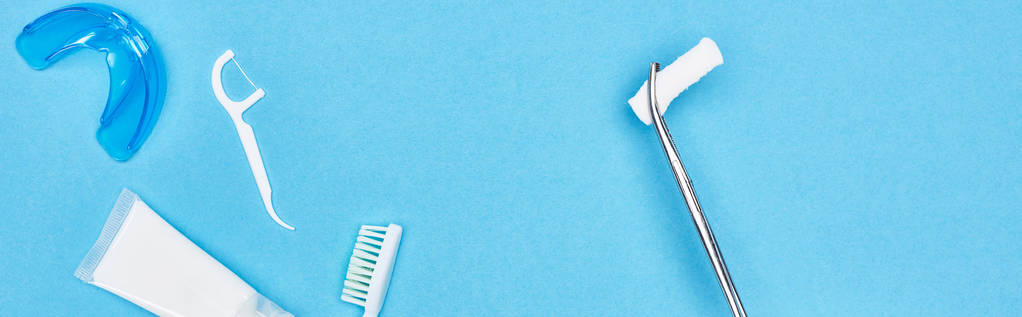 plano panorámico de pinzas con almohadilla de algodón cerca de pasta de dientes y cepillo de dientes en azul
  - Foto, Imagen