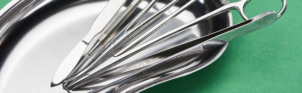 panoramic shot of scissors and dental instruments in metallic plate isolated on green  - Photo, Image