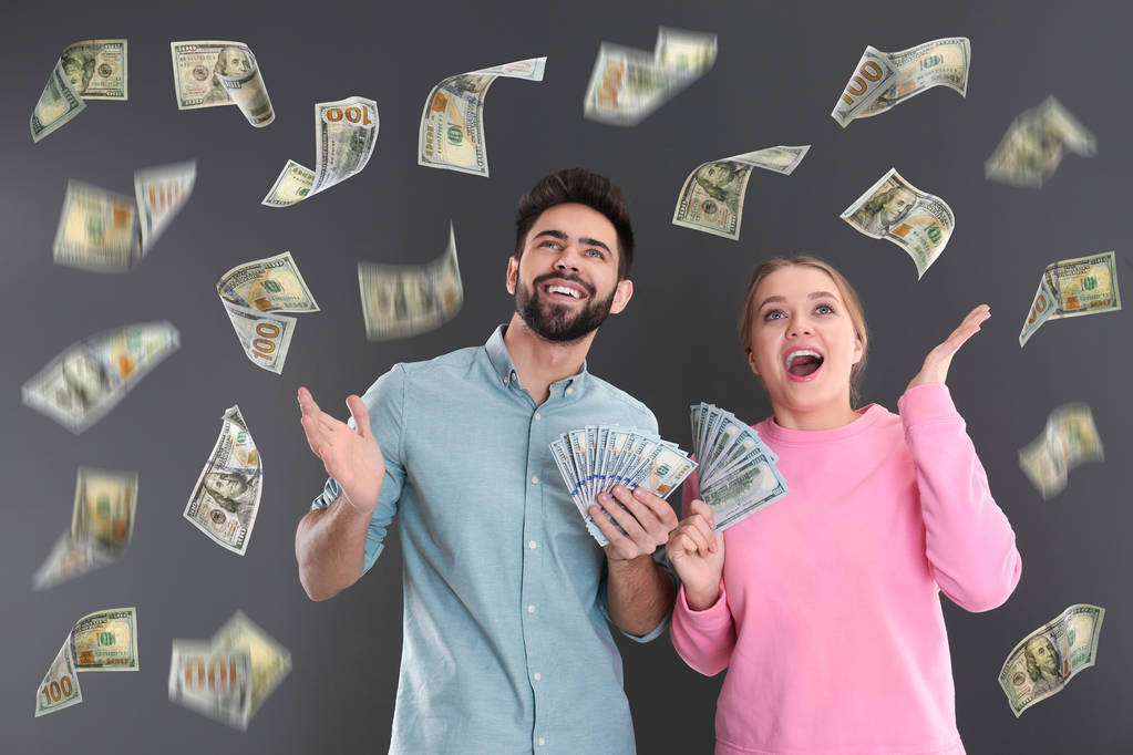 Jovem casal feliz com dólares sob chuva de dinheiro em fundo cinza
 - Foto, Imagem
