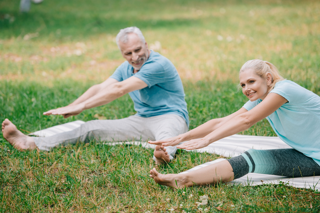 smiling man and woman practicing stretching yoga poses while sitting on yoga mats - Photo, Image
