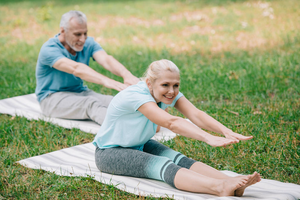 souriant mature homme et femme pratiquant des poses de yoga tout en étant assis sur des tapis de yoga
 - Photo, image