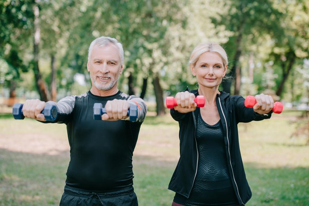 smiling mature sportsman and sportswoman doing exercises with barbells and smiling at camera - Photo, Image