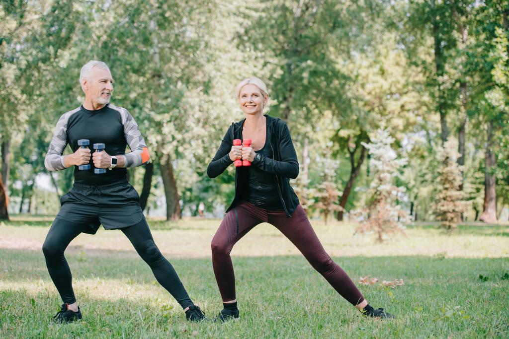 mature sportsman and sportswoman exercising with dumbbells in park - Photo, Image