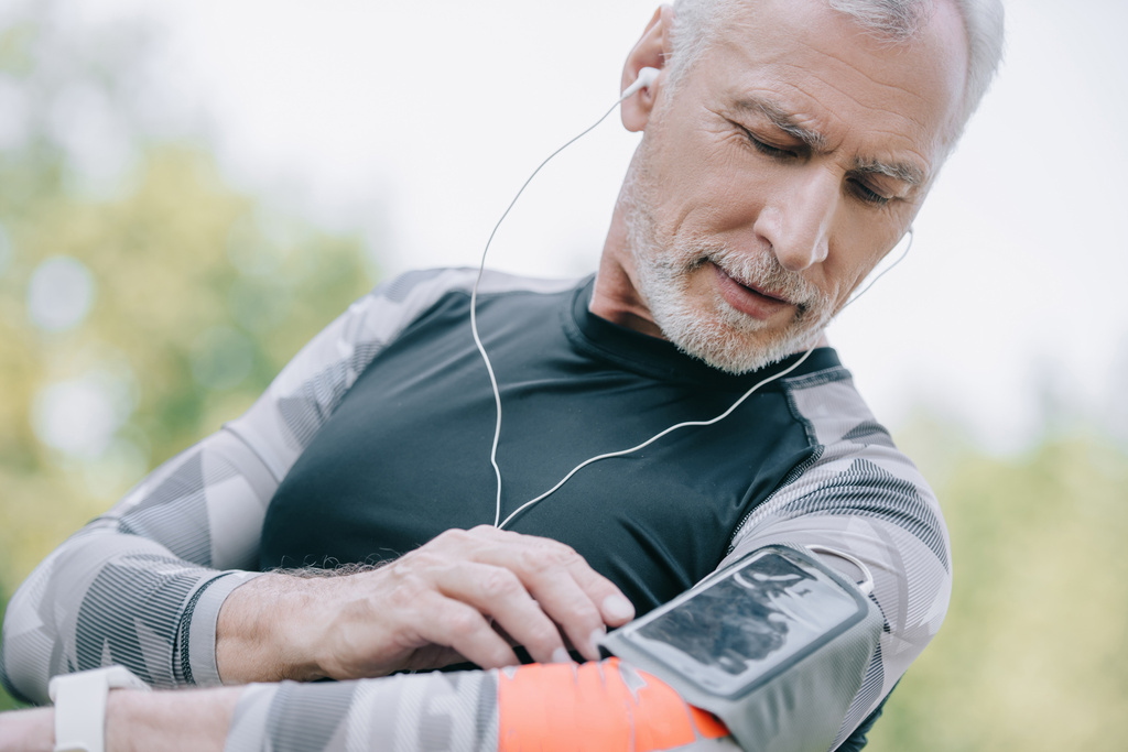 handsome mature sportsman using smartphone in armband case and listening music in earphones - Photo, Image