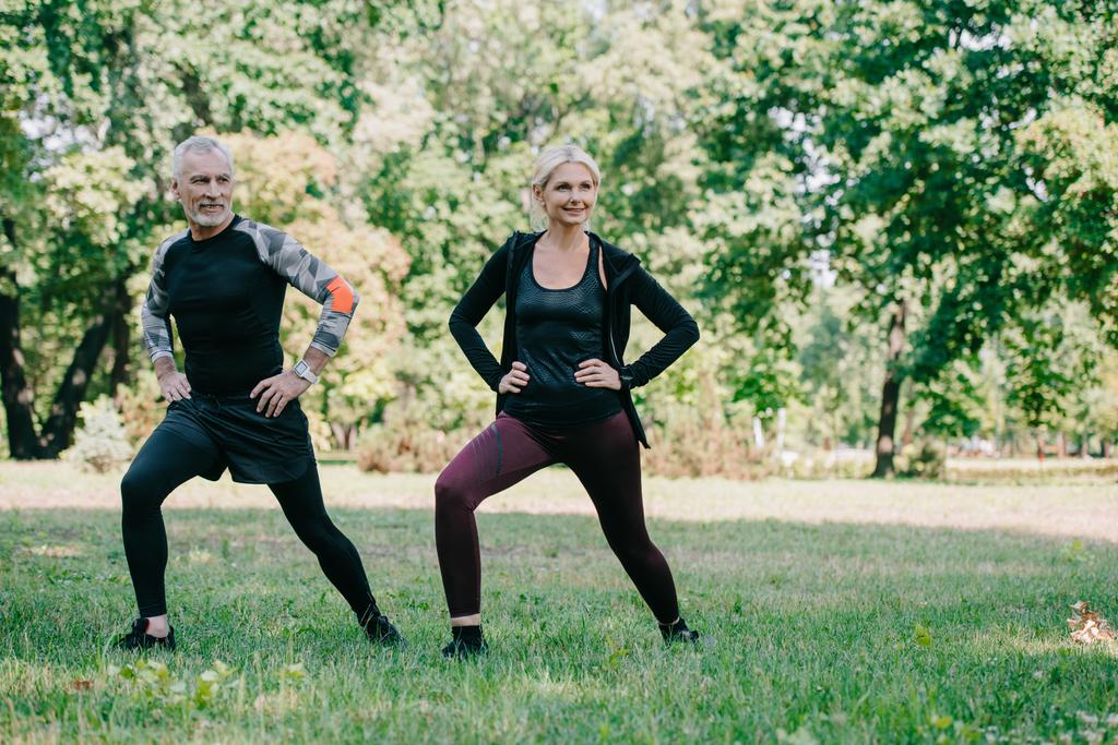 cheerful, mature sportsman and sportswoman doing lunges exercises in park - Photo, Image
