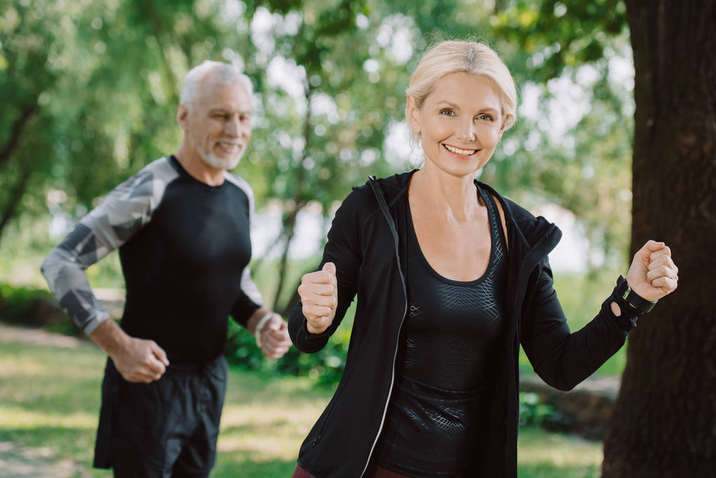 cheerful mature sportsman and sportswoman jogging in park together - Photo, Image
