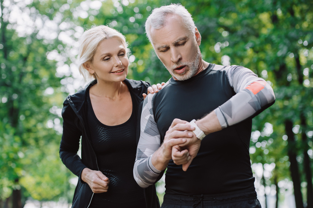 surprised mature sportsman looking at fitness tracker near smiling sportswoman - Photo, Image