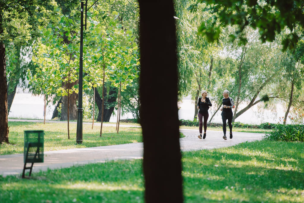 selective focus of mature sportsman and sportswoman jogging together in park - Photo, Image