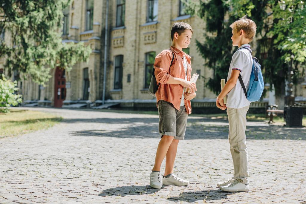 deux écoliers mignons tenant des livres et parlant tout en se tenant dans la cour d'école
 - Photo, image