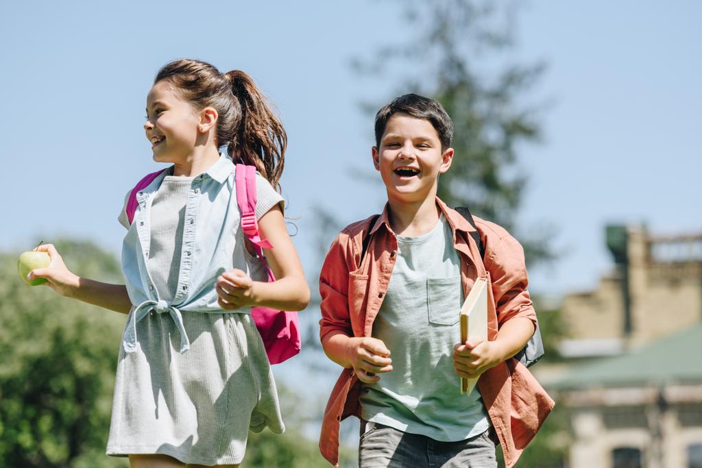 公園で走っている間に笑顔のバックパックを持つ2人の幸せな小学生 - 写真・画像