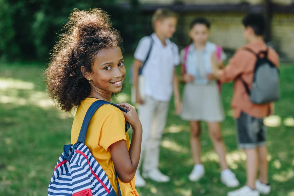szelektív középpontjában az imádnivaló afro-amerikai iskoláslány mosolyogva a kamera közelében többnemzetiségű barátok - Fotó, kép