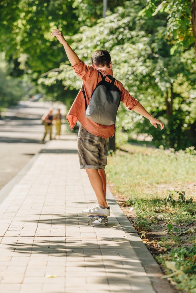 visão traseira do estudante com mochila andar de skate na rua ensolarada
 - Foto, Imagem