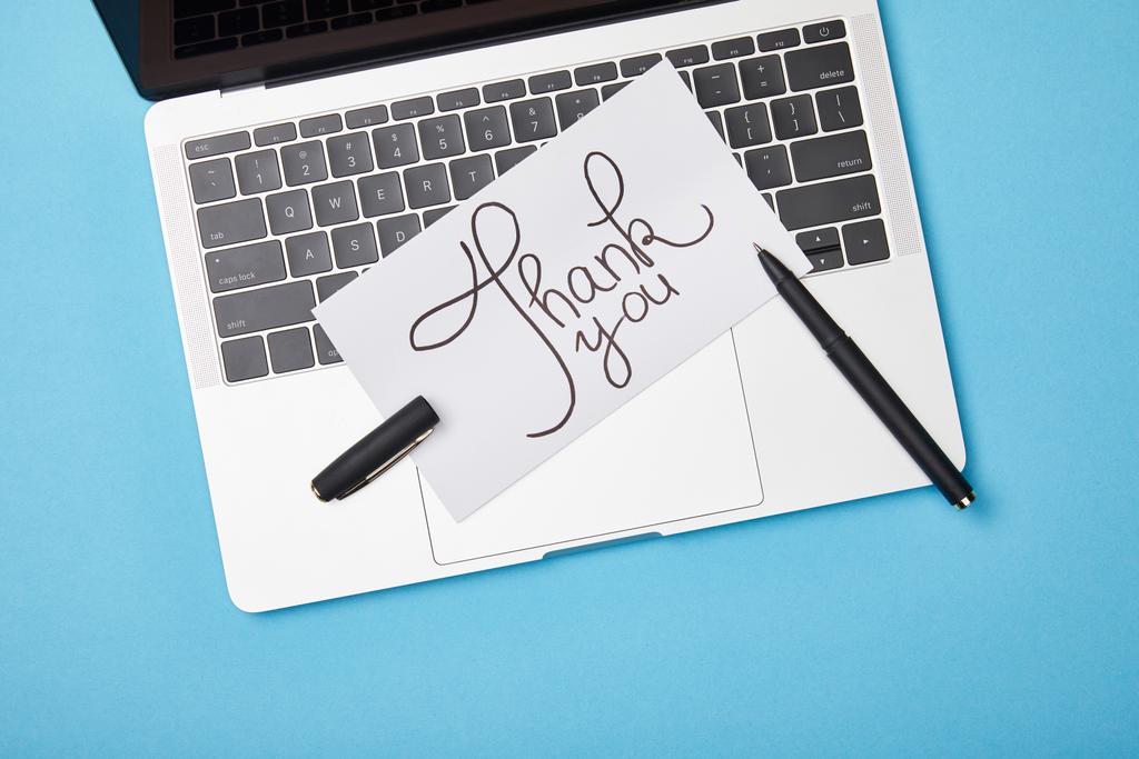 top view of laptop and card with thank you lettering and pen on blue background - Photo, Image