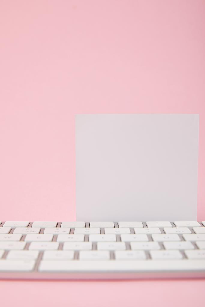 Nahaufnahme der leeren weißen Karte in der Nähe der Computertastatur auf rosa Hintergrund - Foto, Bild