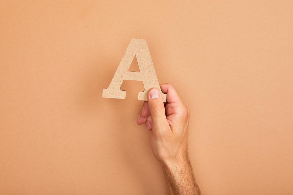 abgeschnittene Ansicht eines Mannes mit einem Buchstaben a auf beigem Hintergrund - Foto, Bild