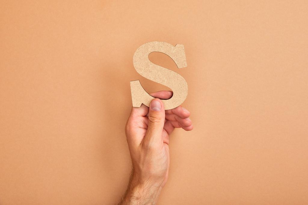 vista parcial del hombre sosteniendo papel cortado letra S sobre fondo beige
 - Foto, Imagen