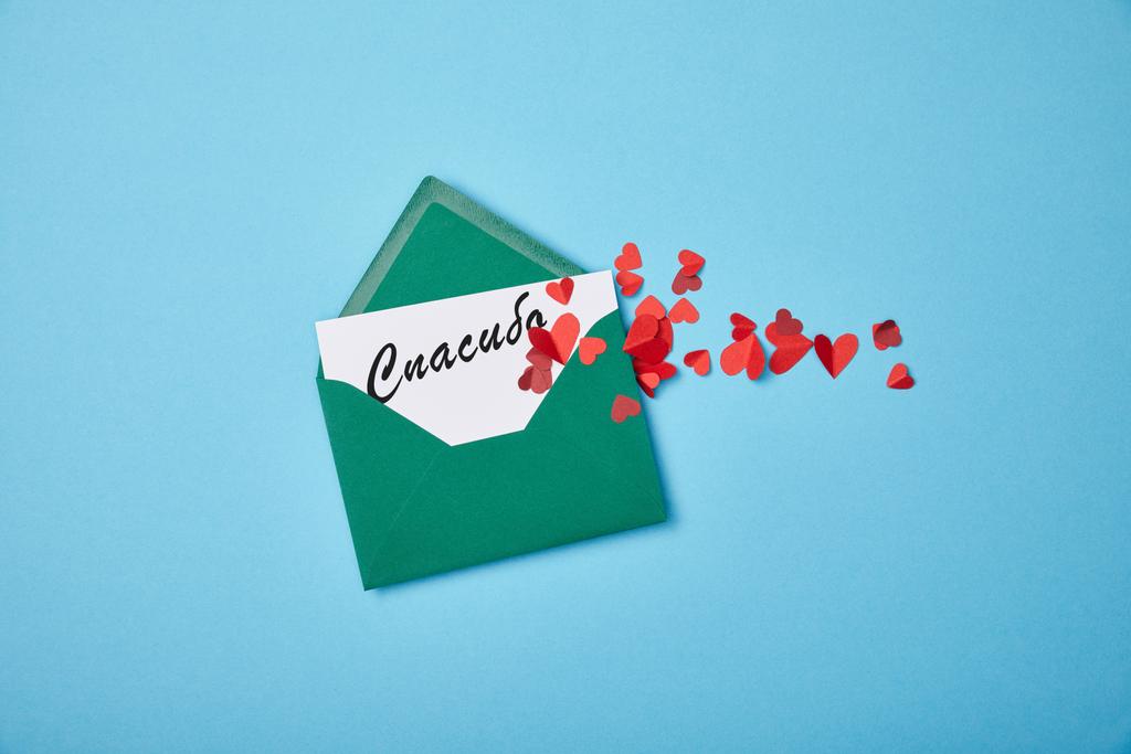 sobre verde con letras de agradecimiento en ruso sobre tarjeta blanca y corazones de papel rojo sobre fondo azul
 - Foto, Imagen