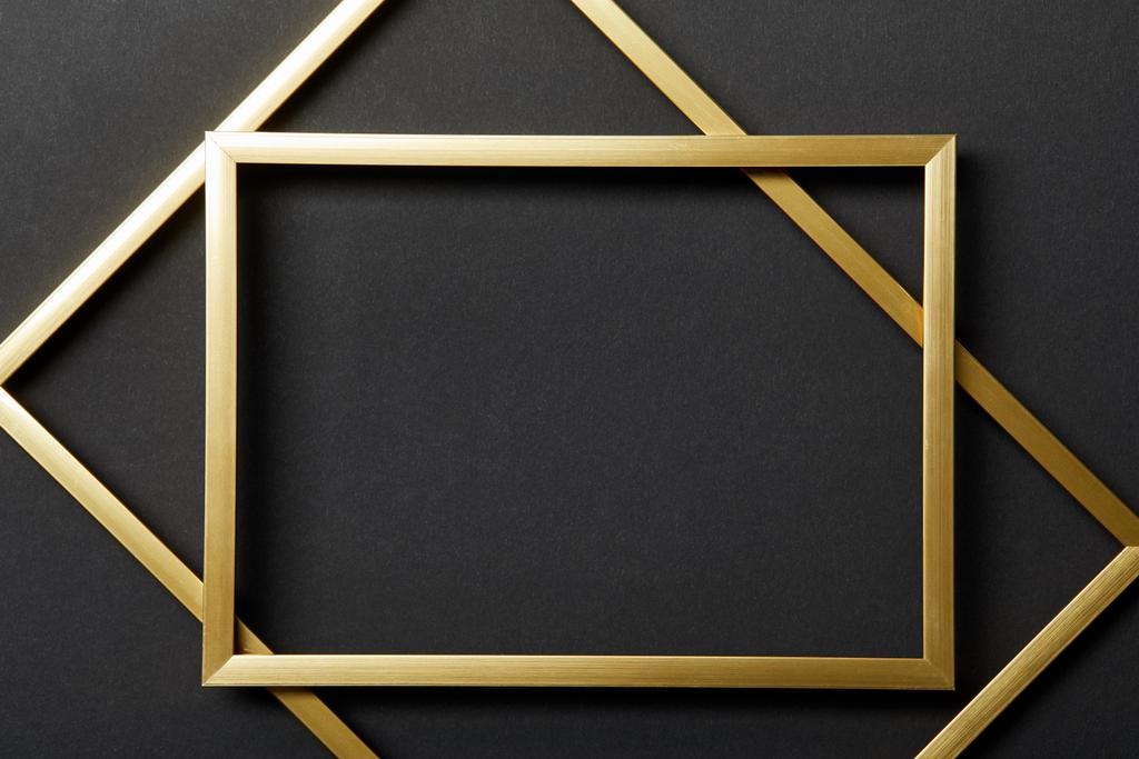 Draufsicht auf leere goldene Rahmen auf schwarzem Hintergrund - Foto, Bild