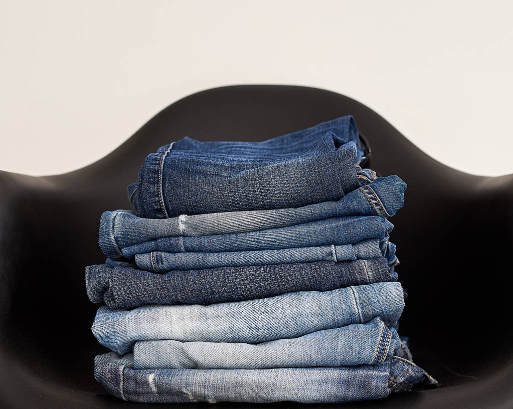 Roupas de jeans empilhadas em uma cadeira de plástico
 - Foto, Imagem