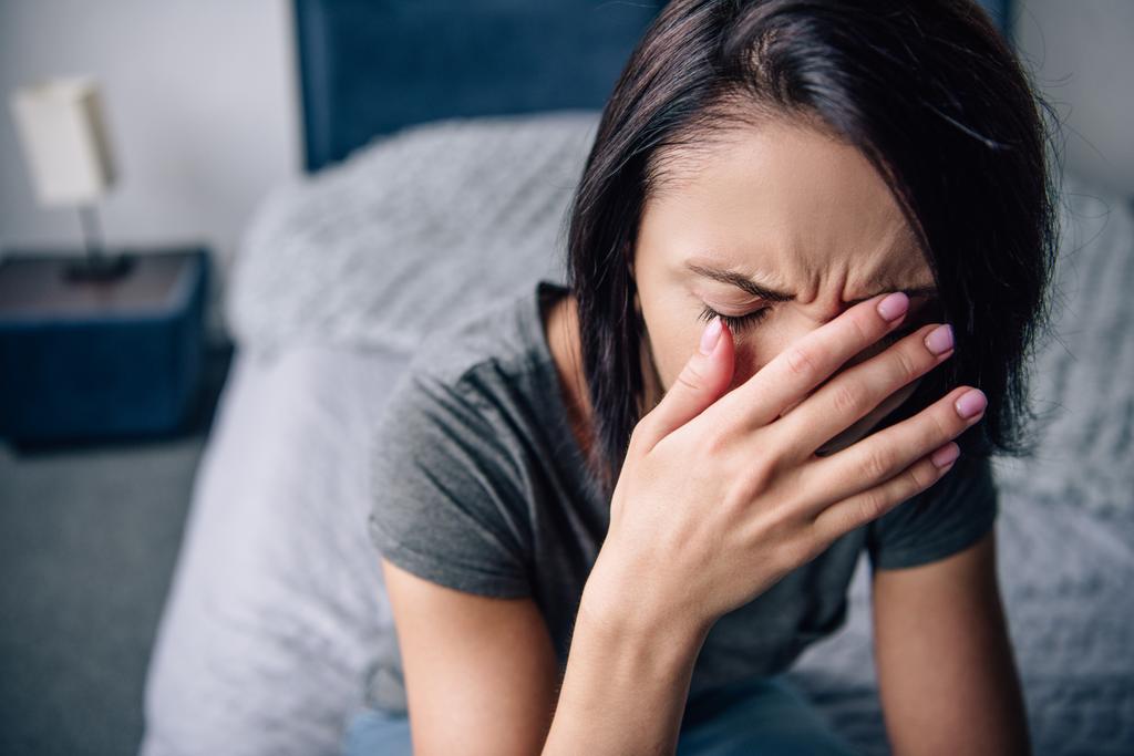 depressive Frau, die zu Hause auf dem Bett sitzt, weint und das Gesicht mit Händen bedeckt - Foto, Bild