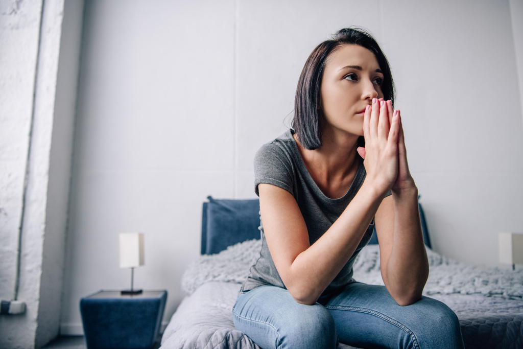 beautiful depressed woman sitting on bed and covering mouth at home - Photo, Image