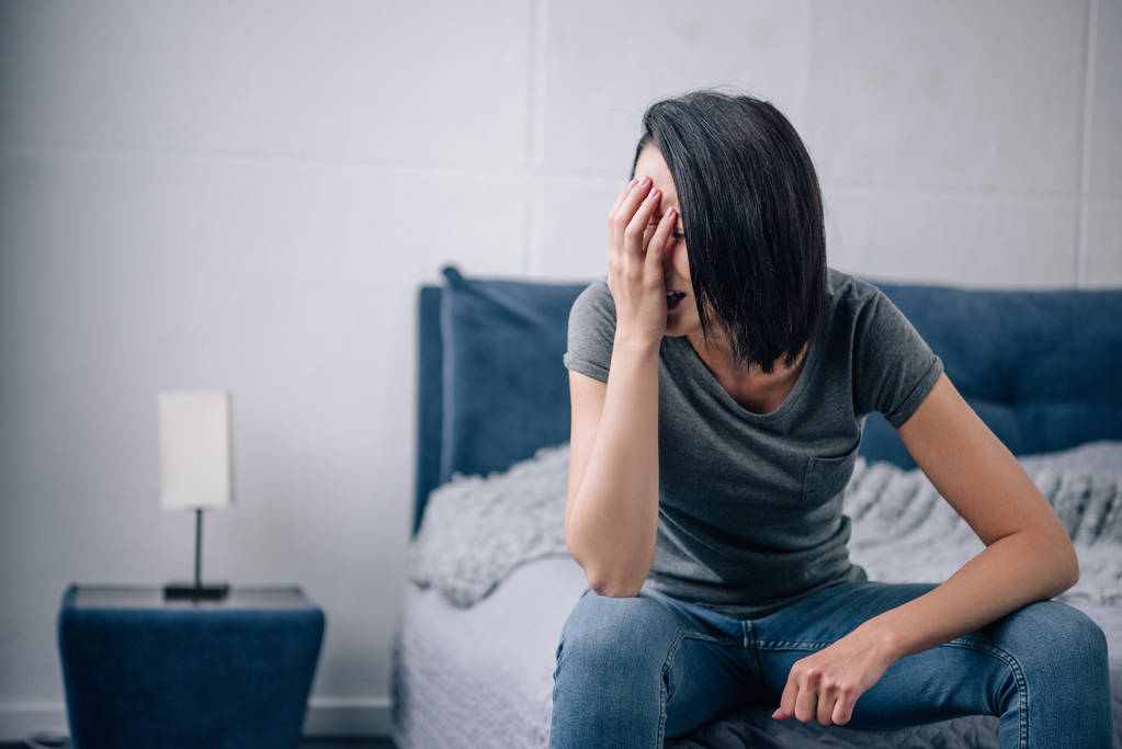 θλιμμένη γυναίκα κάθεται στο κρεβάτι στο σπίτι και κλαίει - Φωτογραφία, εικόνα