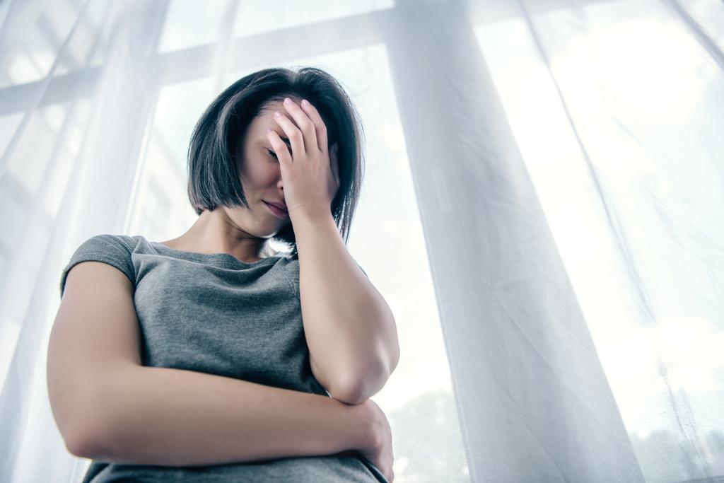 nízký úhel pohledu na depresivní ženu pokrývající obličej doma - Fotografie, Obrázek