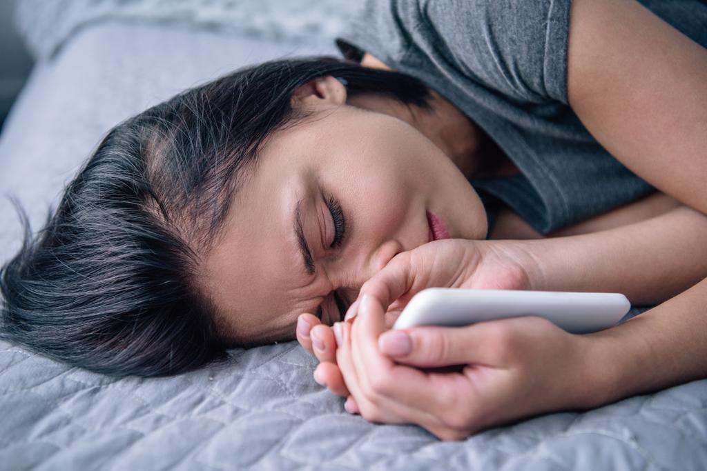 mujer deprimida solitaria acostada en la cama y sosteniendo el teléfono inteligente en el dormitorio
 - Foto, imagen