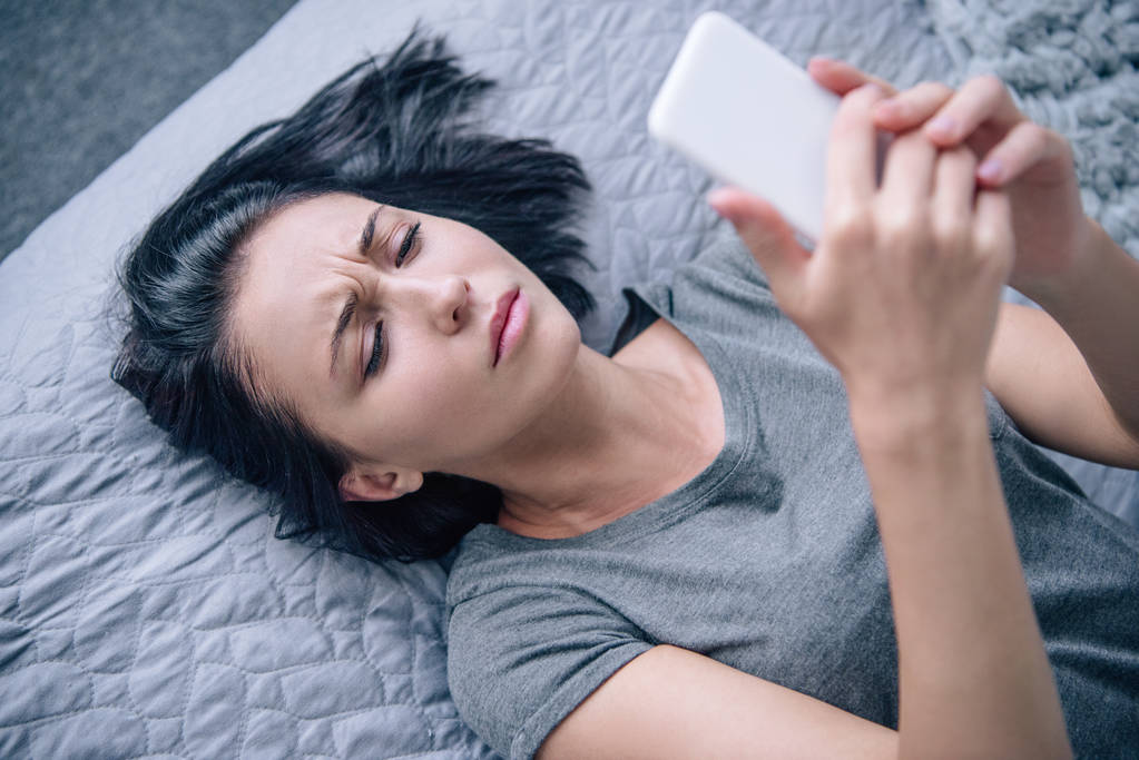 mooie depressieve vrouw op bed met smartphone in de slaapkamer - Foto, afbeelding