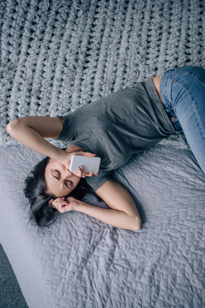 вид сверху на депрессивную женщину на кровати со смартфоном в спальне
 - Фото, изображение