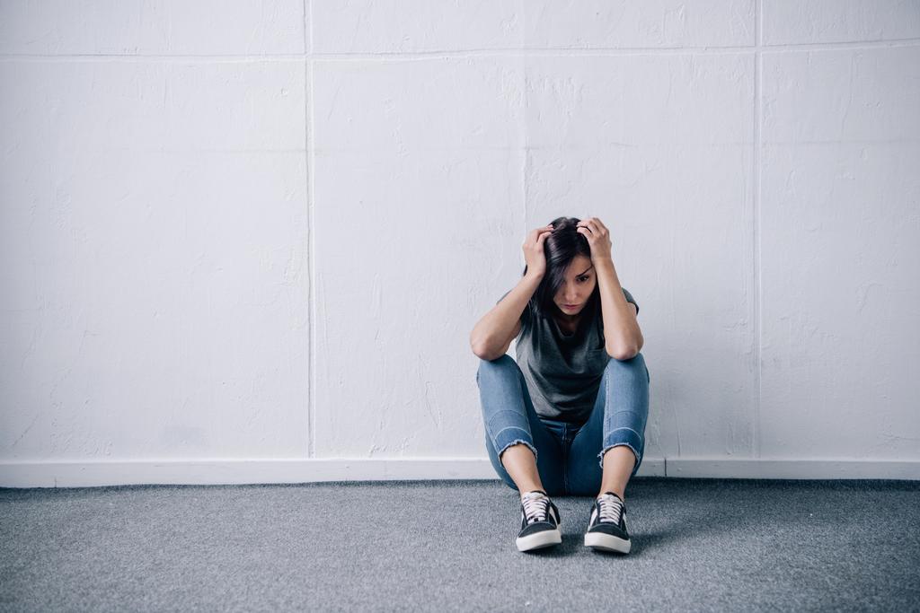 depresja Samotna kobieta brunetka z rękami na głowie siedzi na podłodze w domu - Zdjęcie, obraz