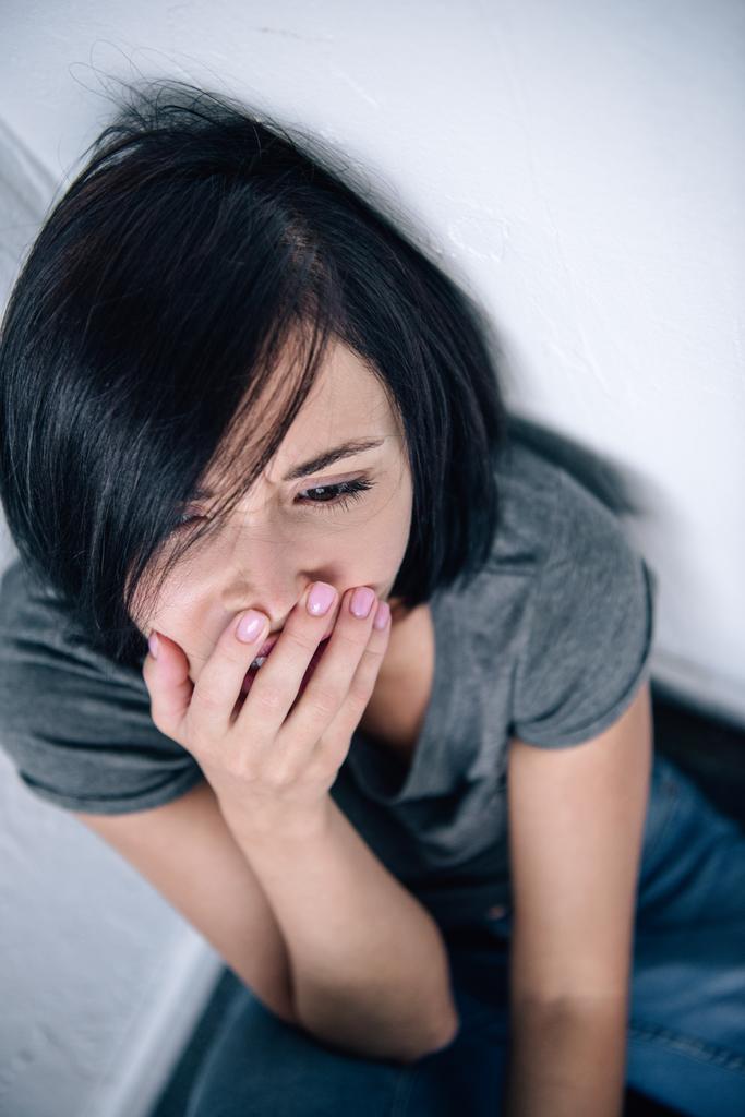 high angle view of depressed brunette woman covering mouth at home - Photo, Image