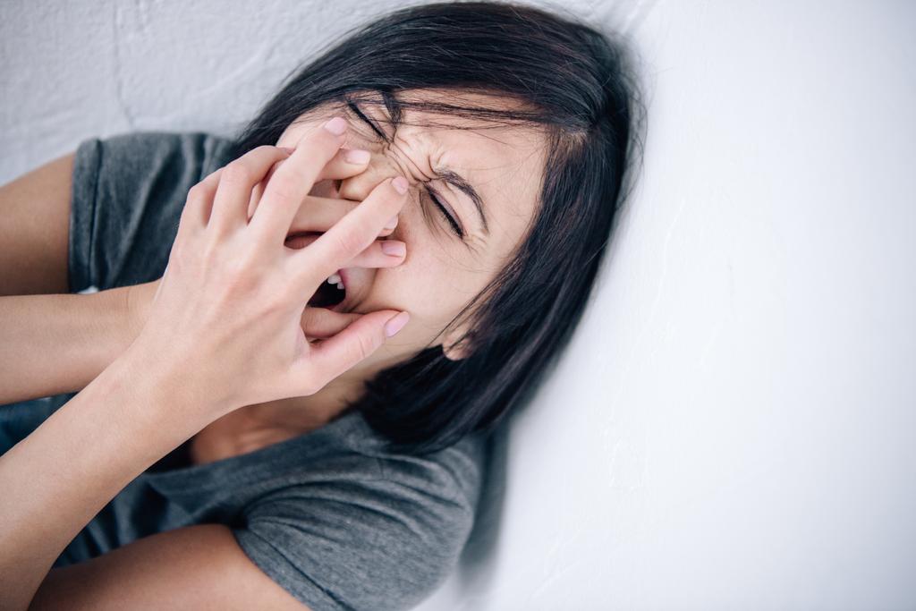 depressieve brunette vrouw bedekt mond en schreeuwen thuis - Foto, afbeelding