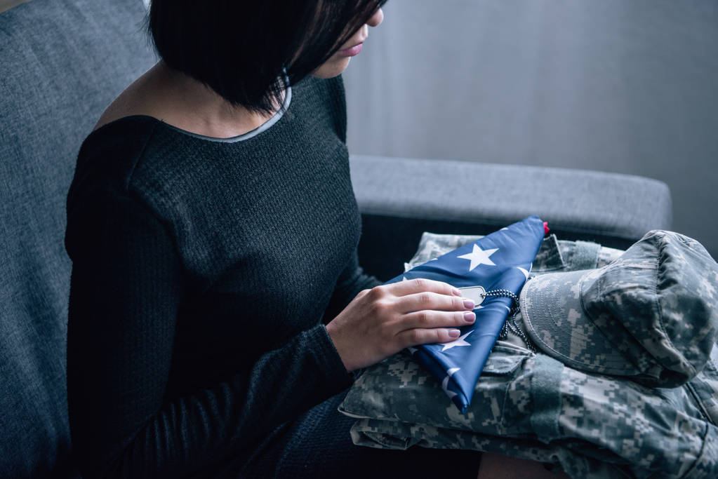 vue recadrée de la femme sur le canapé avec des vêtements militaires et le drapeau américain foded à la maison
 - Photo, image