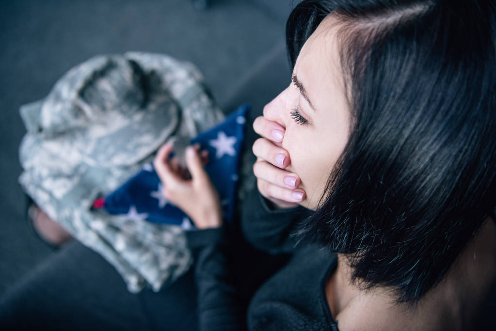 depressive Frau mit Militärkleidung, die den Mund bedeckt und zu Hause weint - Foto, Bild