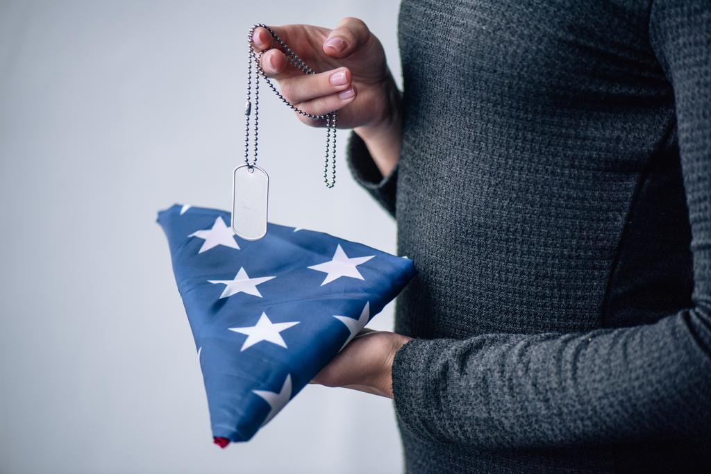 タグ犬を持つ女性のトリミングされたビューと自宅で折り畳まれたアメリカの旗 - 写真・画像