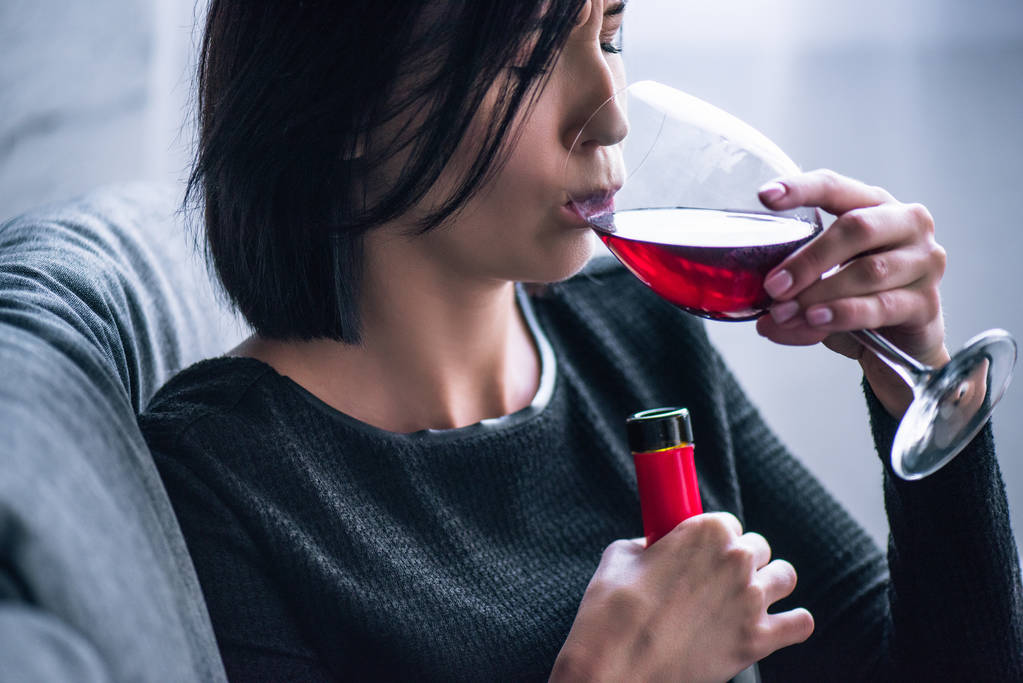 подавленная женщина сидит на диване и пьет вино дома
 - Фото, изображение