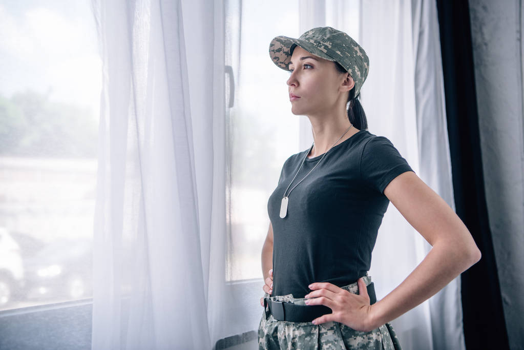 piękna kobieta z ręki na biodrze w mundurze wojskowym w domu z kopią przestrzeni - Zdjęcie, obraz