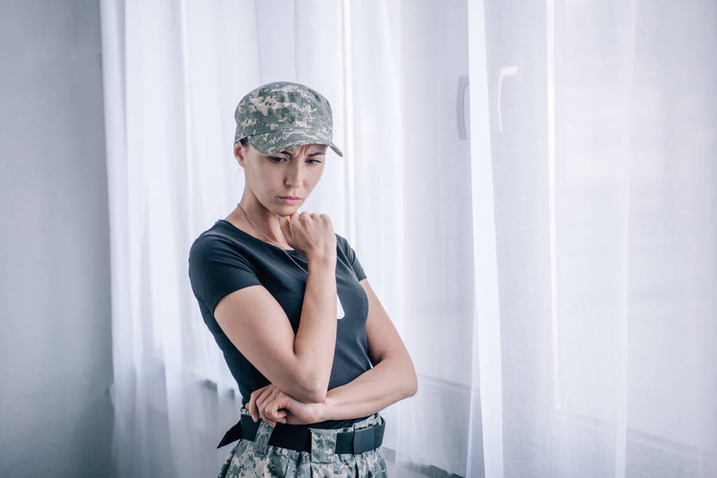 depressive, nachdenkliche Frau in Militäruniform, die zu Hause das Kinn berührt - Foto, Bild