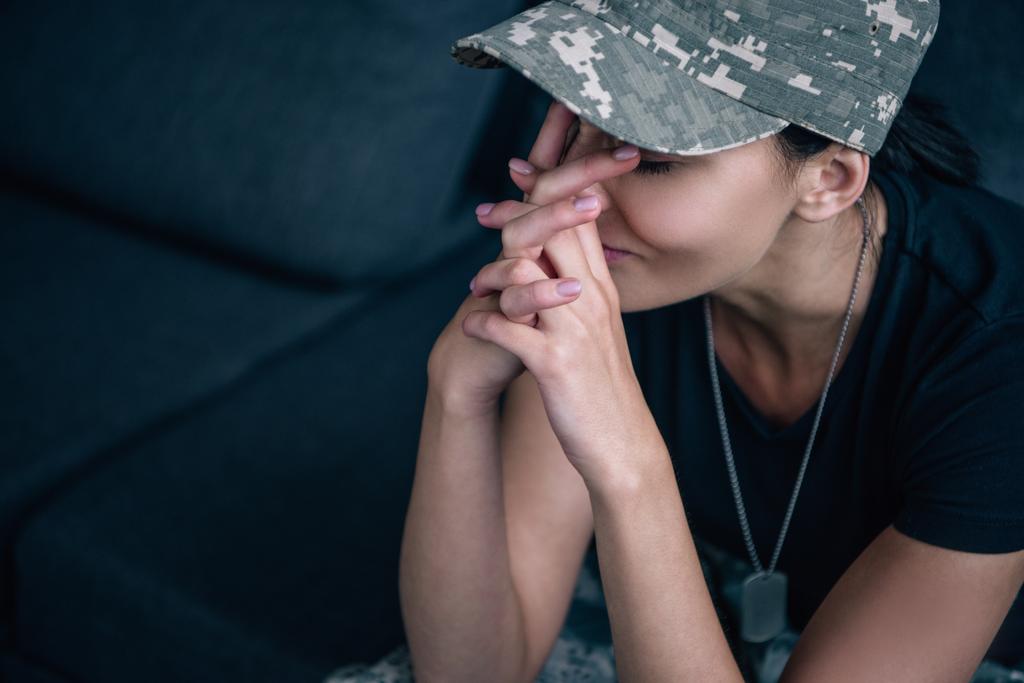 donna depressa in uniforme militare seduta sul divano con le mani serrate a casa
 - Foto, immagini