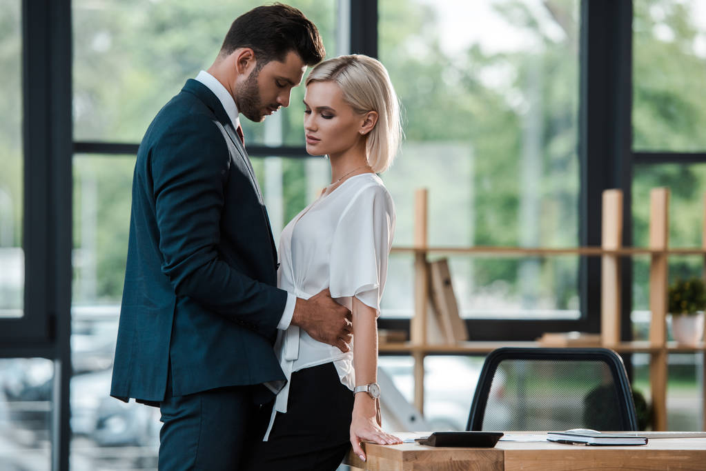 pohledný obchodník dotek atraktivní mladé ženy při flirtování v kanceláři  - Fotografie, Obrázek
