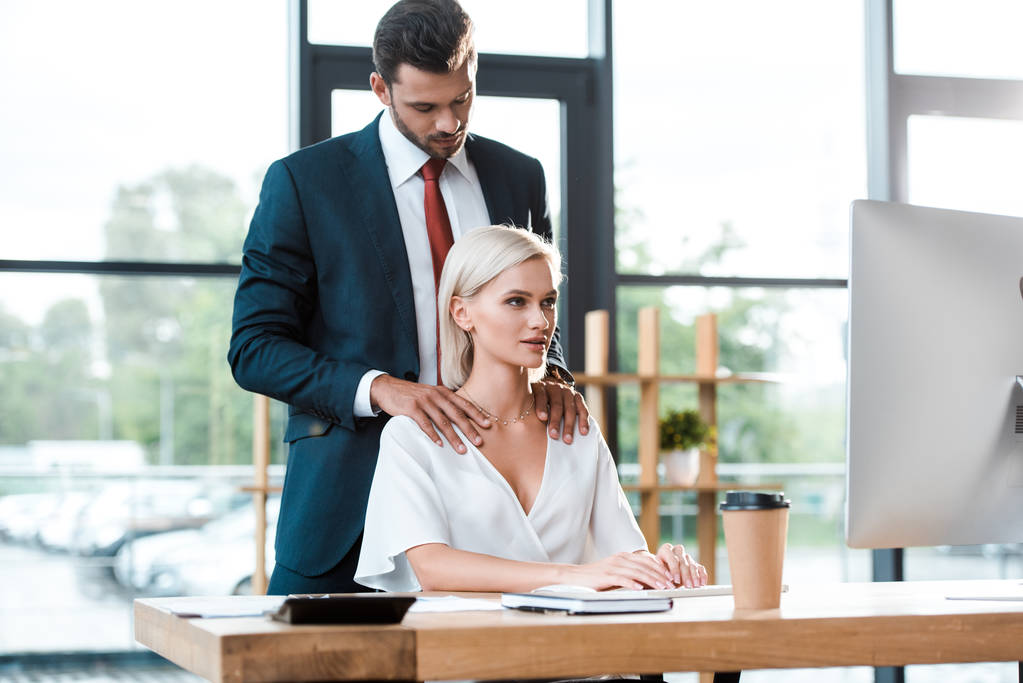 selektivní zaměření hezkého vousatého muže, který se dotýká přitažlivé dívky pracující v kanceláři  - Fotografie, Obrázek